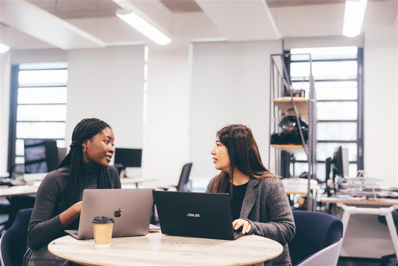Two female students sitting at a table with laptops in front of them