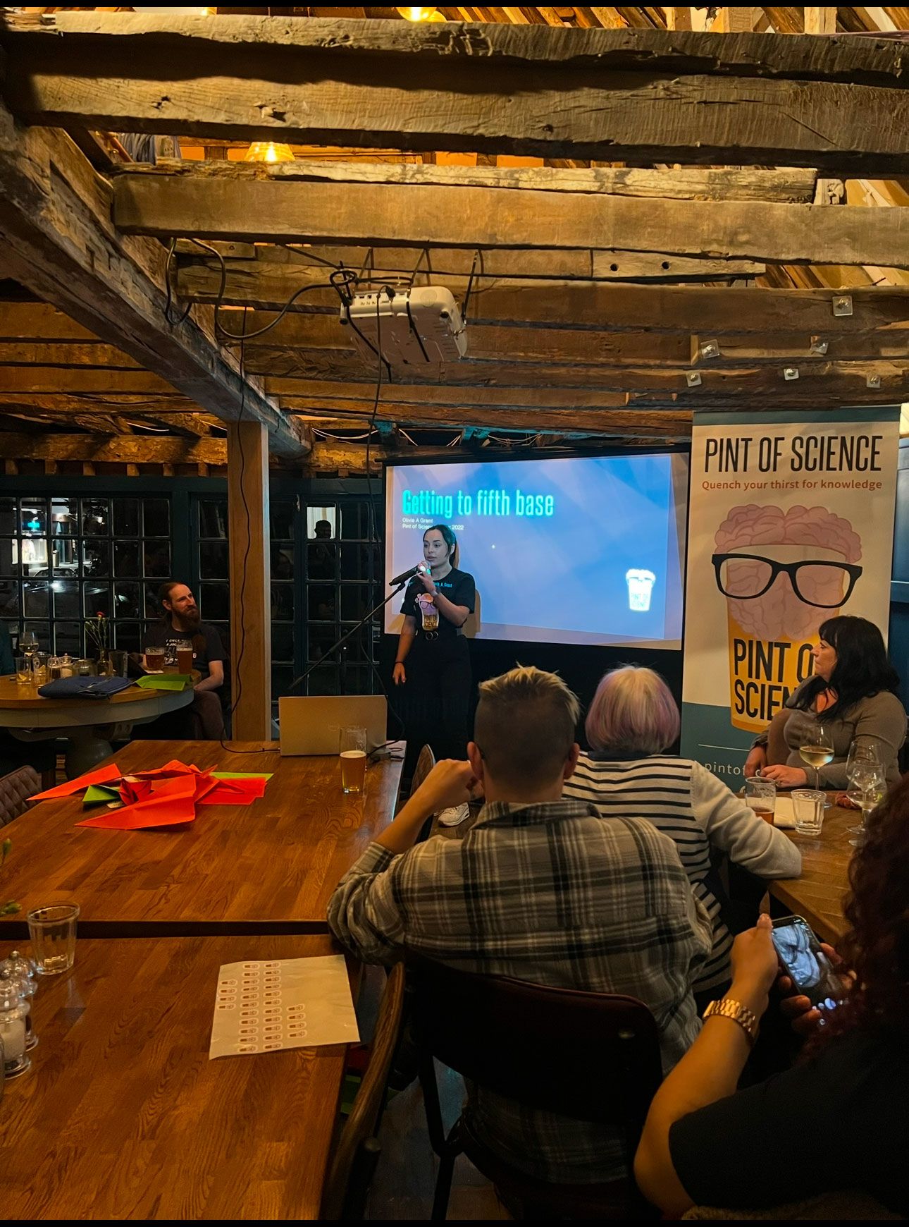Liv stood in front of a screen with a microphone, speaking at a Pint of Science event