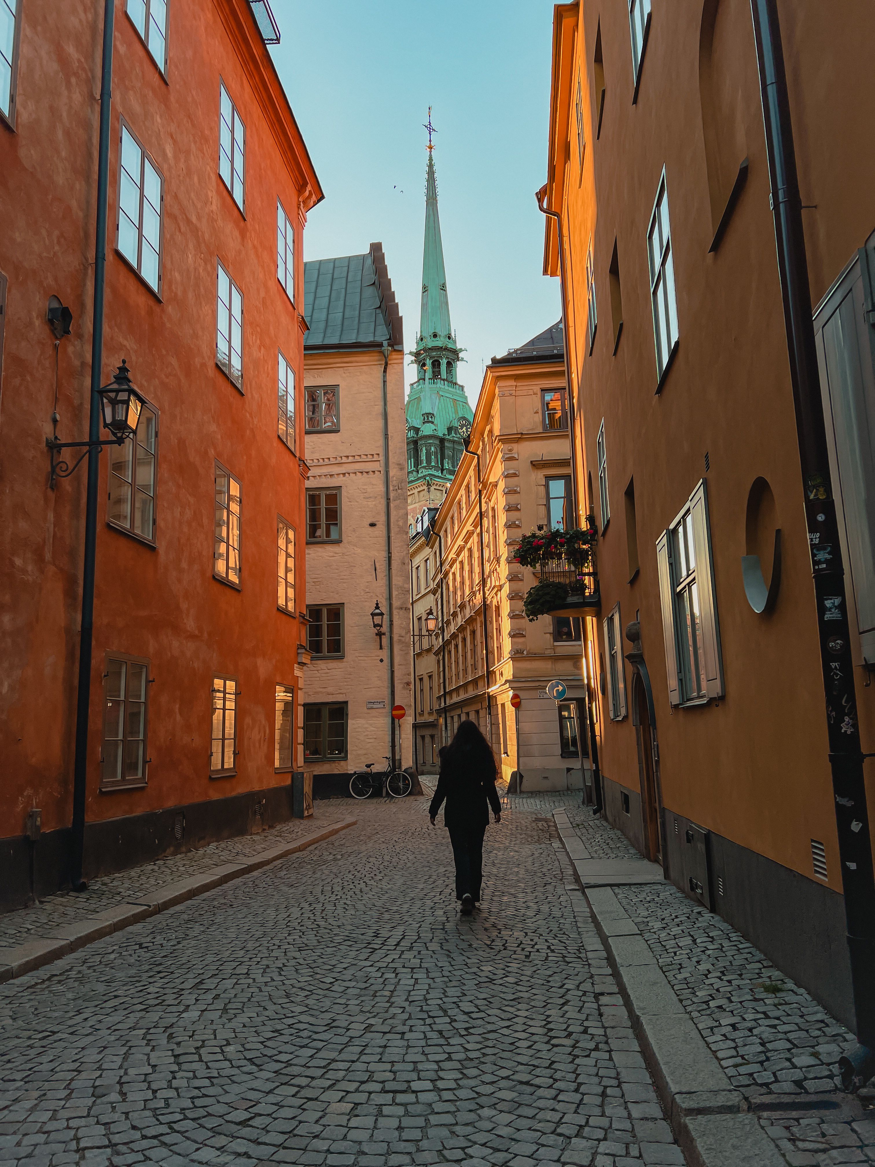 Ela walking the streets of Stockholm. The buildings are old and colourful, the streets are cobbled.