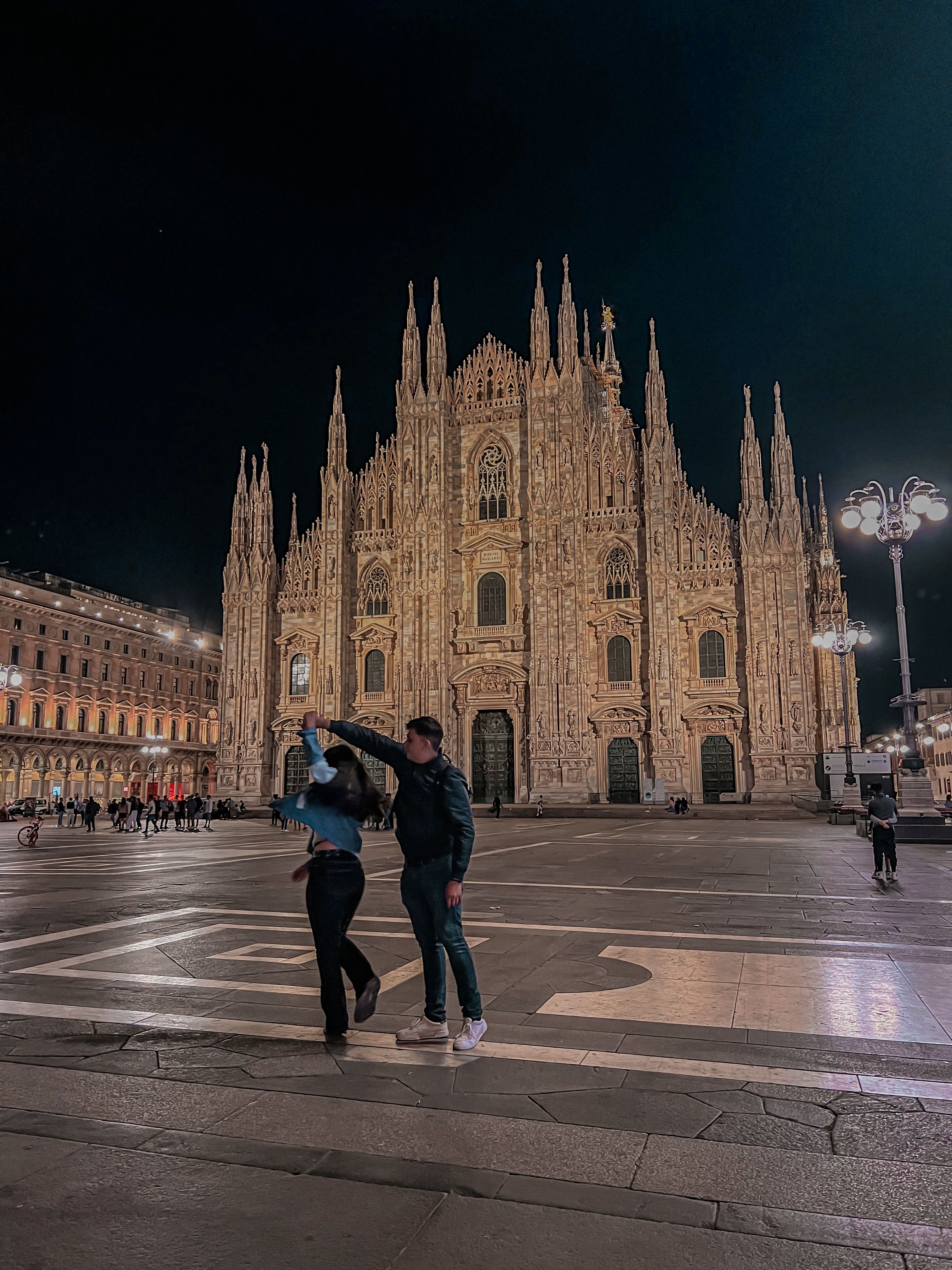 Ela and her partner are dancing hand in hand in front of the Duomo in Milan, it's nighttime and the Duomo is lit