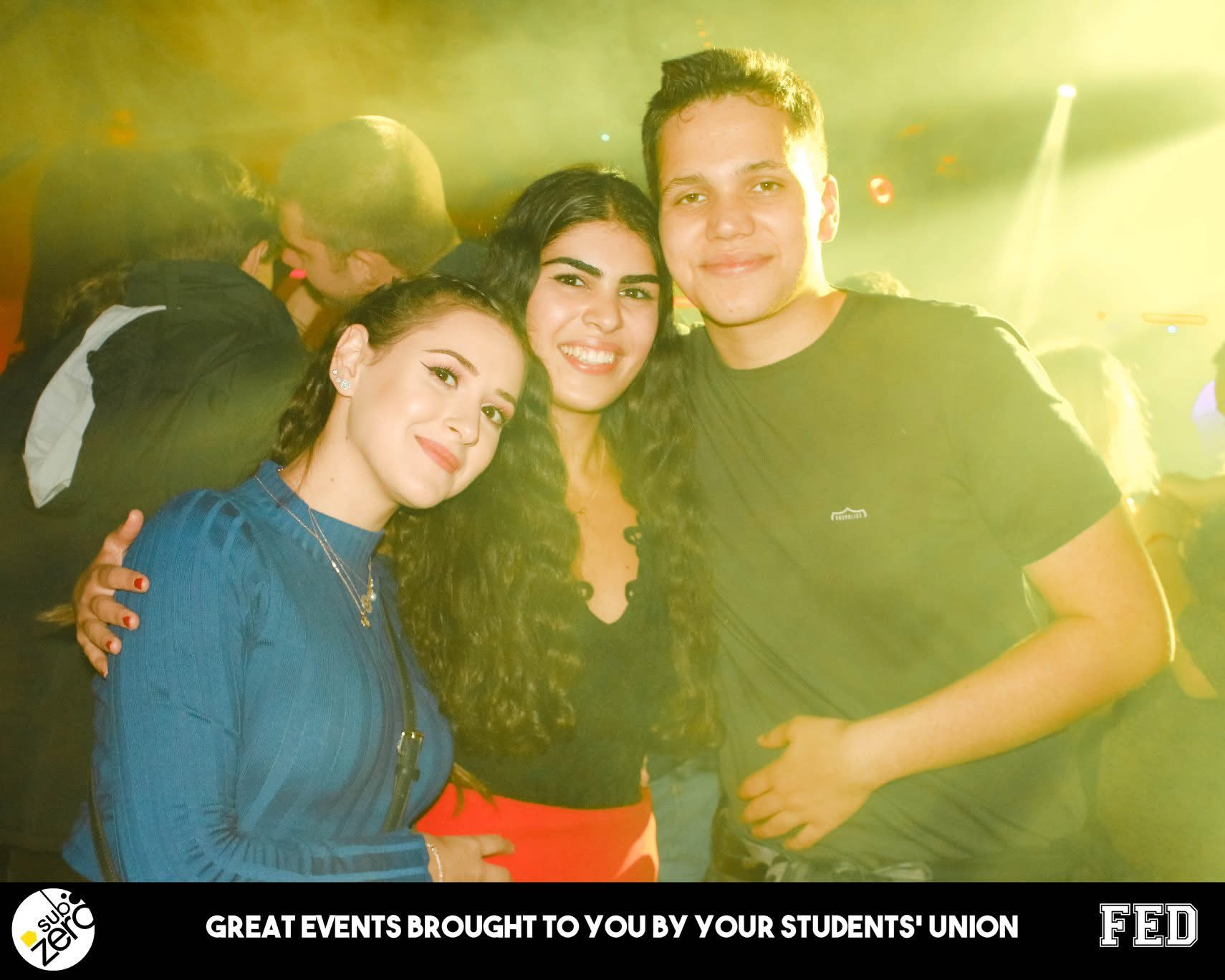 Three students, Ela is in the middle, huddled for a picture in the middle of a nightclub