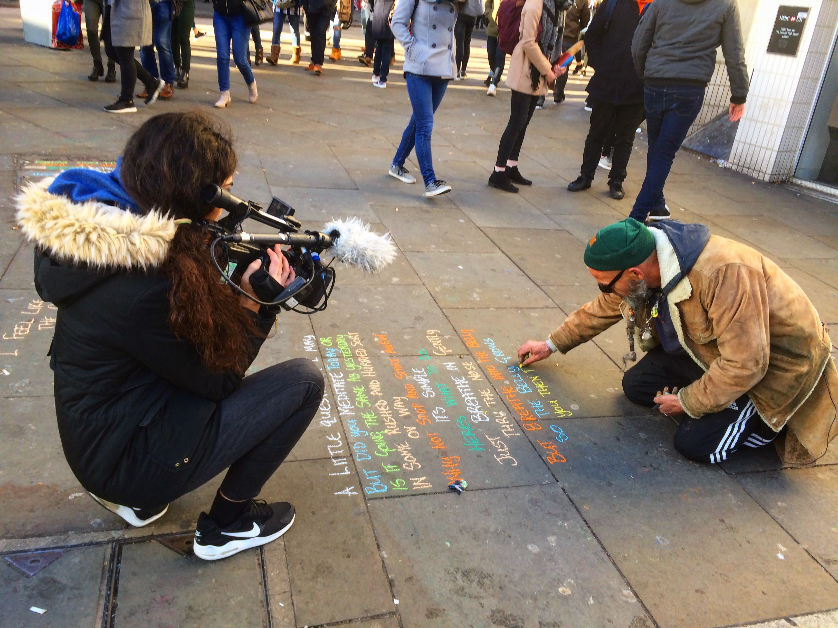 Ela filming a street artist who is using coloured chalks to write on the paved floor