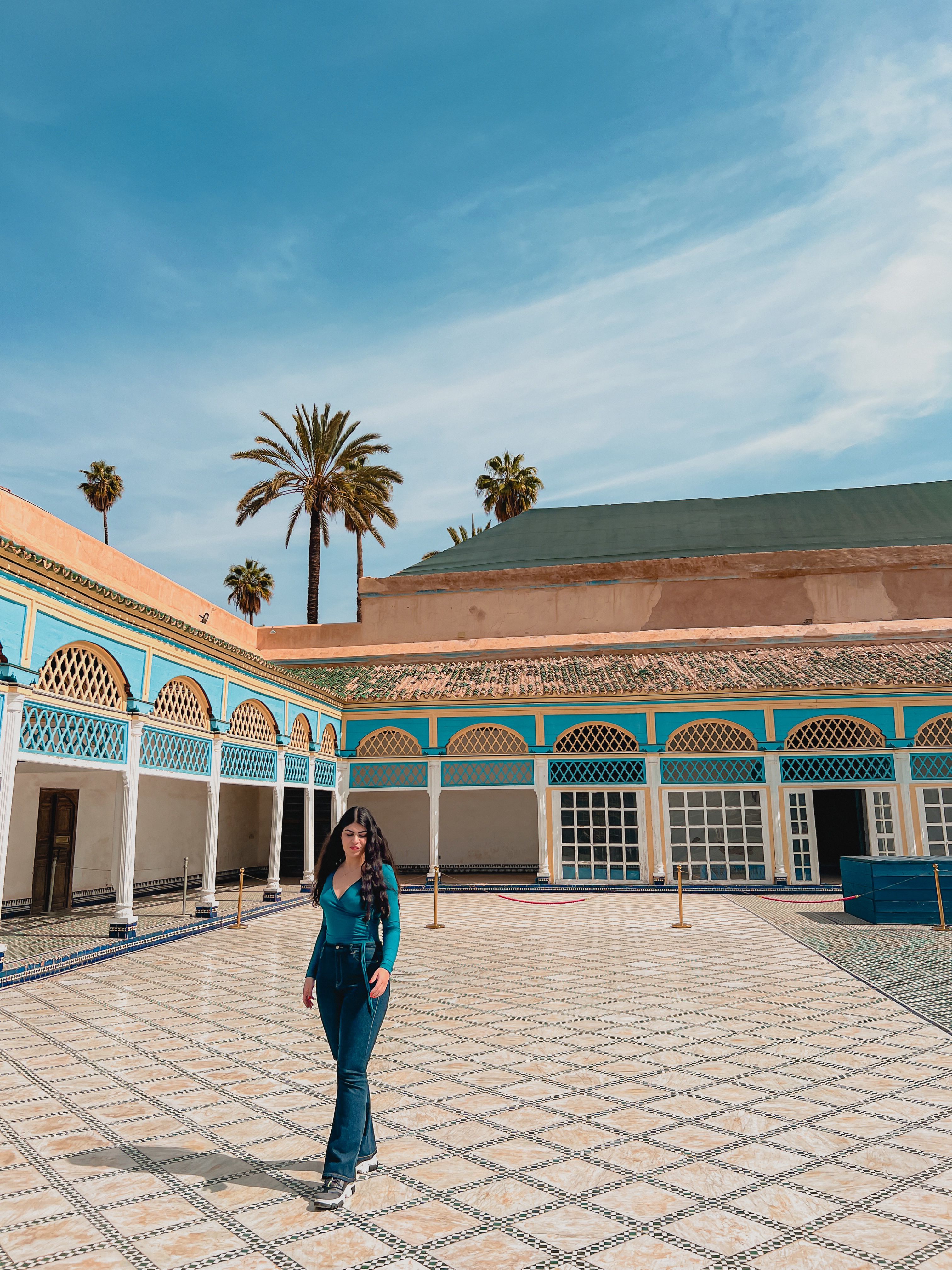Ela is stood in a square in Marrakech, the background is beautifully paved floor and archways with blue paintwork and terracotta 