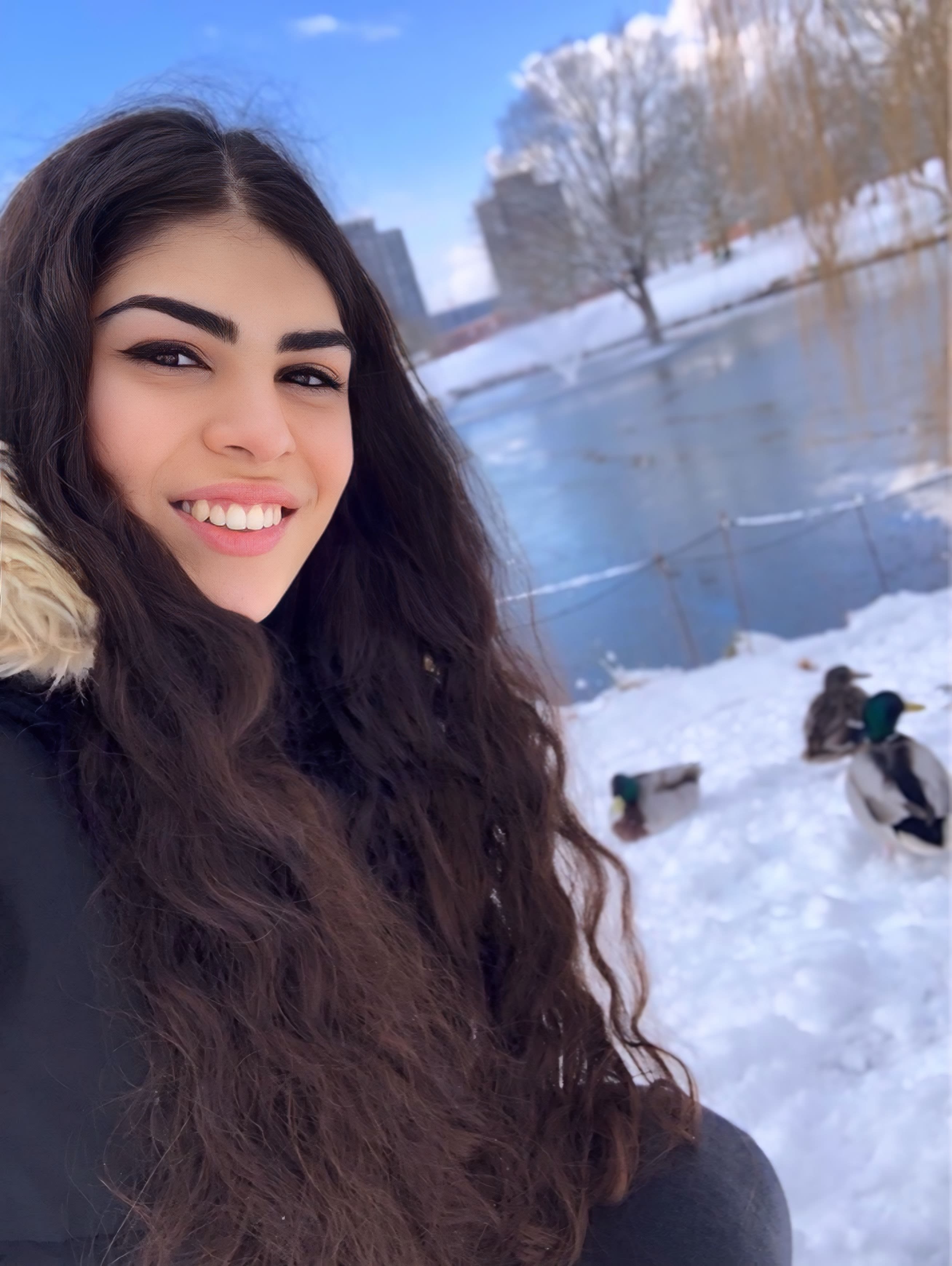 Ela in a warm winter coat with the background showing the Colchester Campus covered in snow