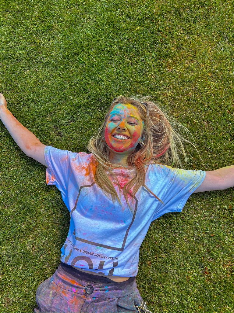 Lily-May laying on the grass covered in paint from holi fest celebrations