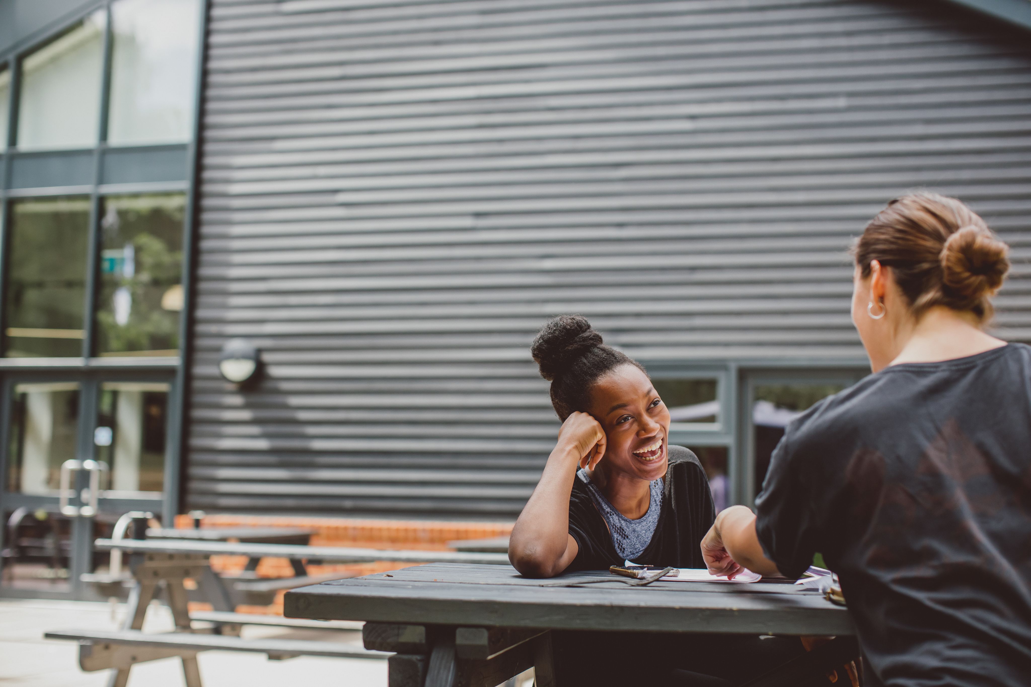 Students laughing, sat at a picnic bench 