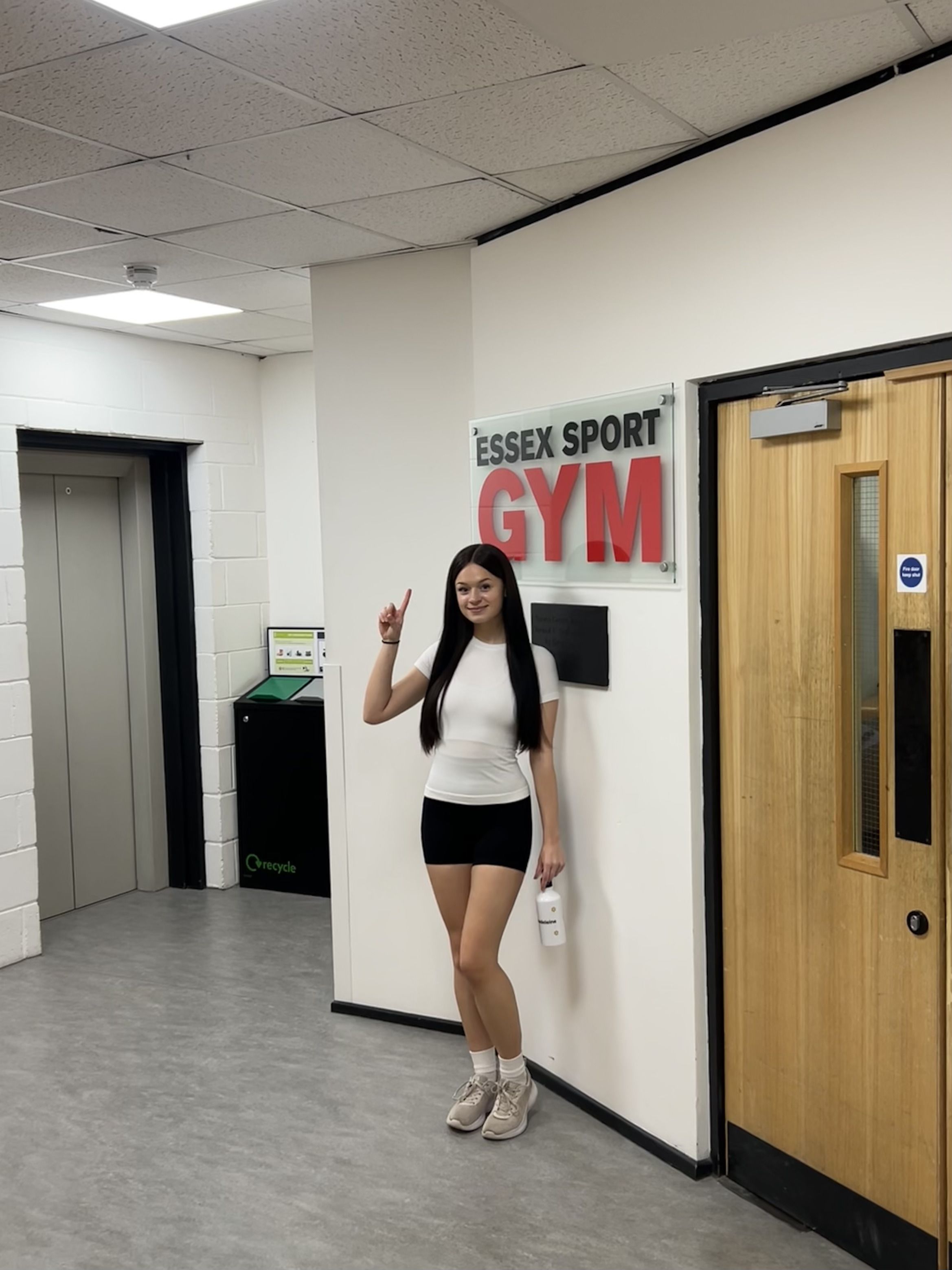 Maddie stood in front of a sign for Essex Sport Gym, pointing at the sign.