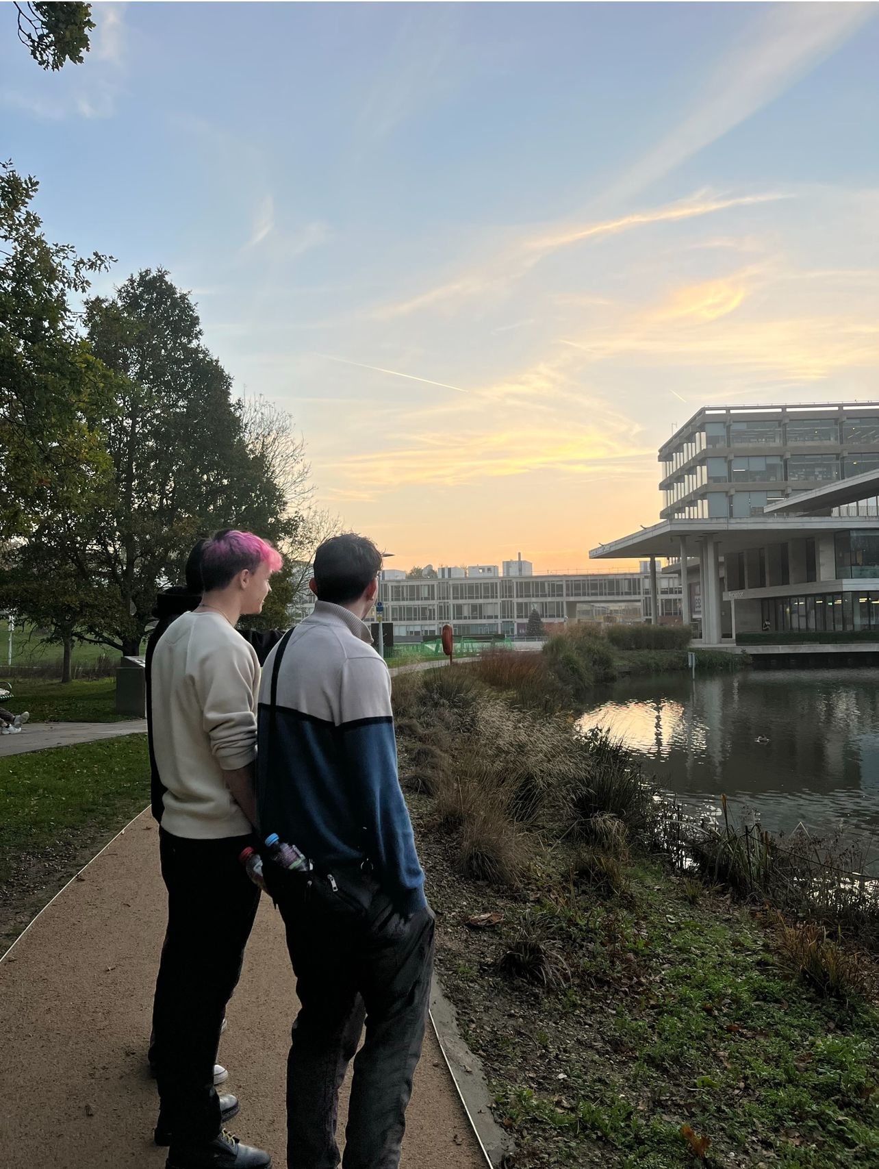 2 students, pictures from behind, looking across the lake towards the library and Silberrad centre