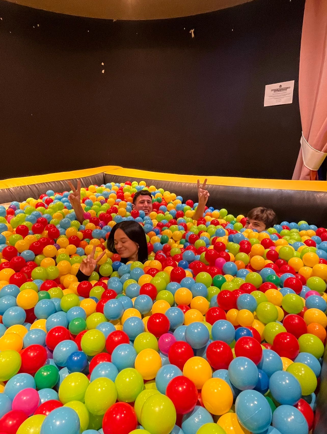 Maddie and 2 friends submerged in a ball pit. They are all laughing.