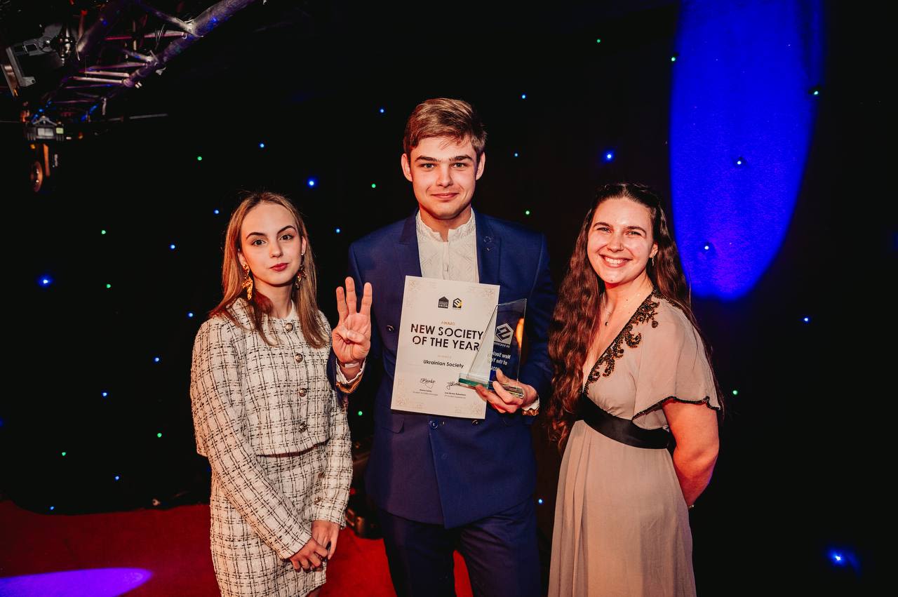 Mark and 2 other students holding an award for "New Society of the Year"