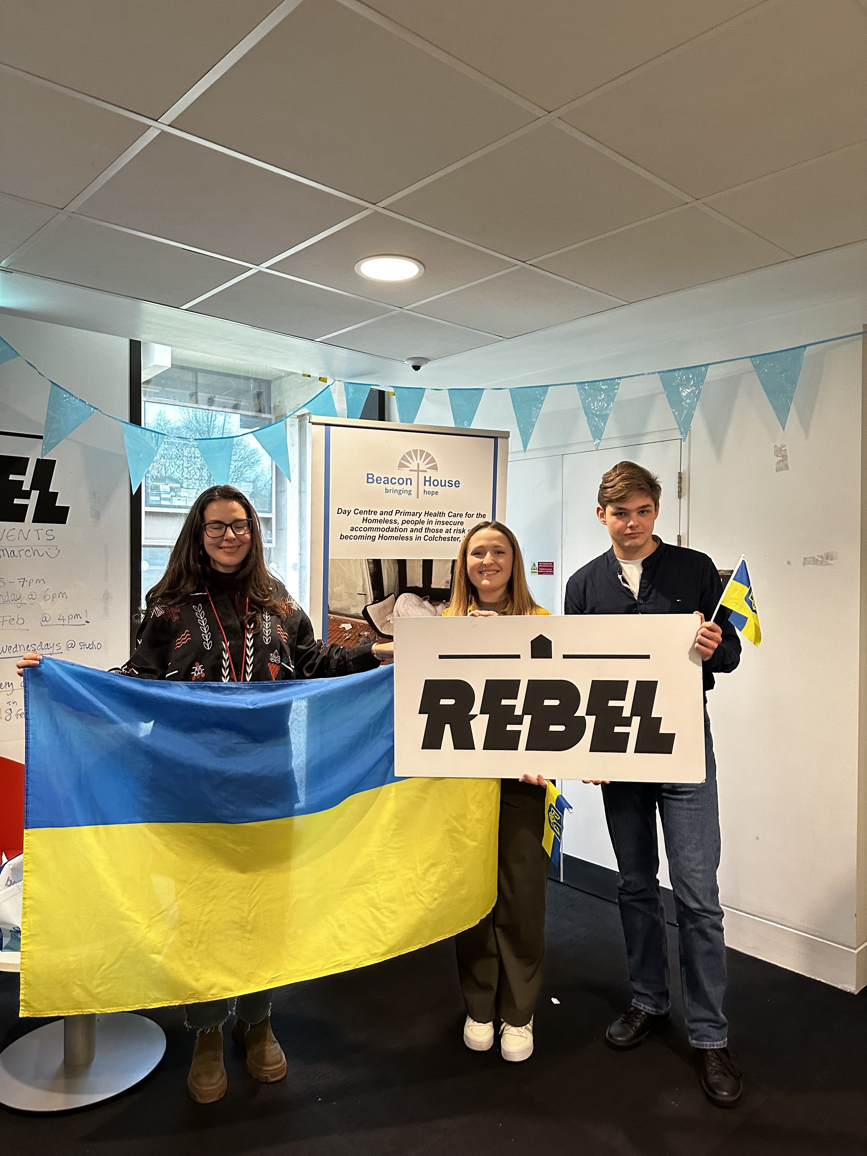 Mark with 2 fellow members of the Ukrainian Society. They are holding a Ukrainian flag and 'Rebel' sign from the Students' Union.