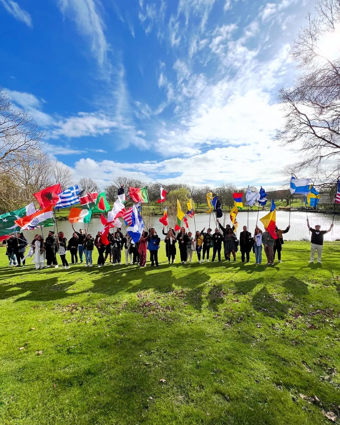 Large group of students in front of the lake all holding different nation's flags